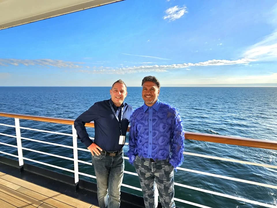 Cruising with Danny and Peter, Holland America Line, Westerdam, Bering Sea, Alaska, United States, Arctic Circle Adventure | A vibrant scene aboard Holland America Line’s Westerdam during the Alaska Arctic Circle Solstice cruise in the Bering Sea, Alaska, United States. Passengers gather around the Lido pool, preparing for the exhilarating Polar Bear Plunge, with crew members setting up the chilled pool to simulate Arctic waters. In the background, stunning Arctic landscapes unfold, featuring pristine ice floes floating on deep blue waters under a golden-hued sky, with distant glaciers and occasional wildlife, such as seals and seabirds, enhancing the untamed beauty of the Frozen Sea Adventure.