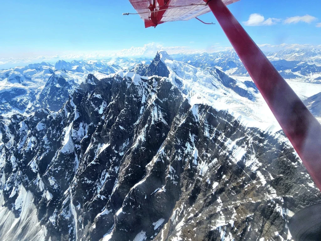 Unforgettable Alaska Flightseeing: A Journey Over Denali National Park 5 Cruising with Danny and Peter, Holland America Line, Westerdam, Anchorage, Alaska, United States | Aerial view of Denali, North America's tallest peak, and the majestic Alaska Range, captured during a Denali National Park flightseeing tour from Anchorage. The image also shows the stunning Ruth Glacier, a specialized plane with skis landing on Denali's snowy terrain, and wildlife such as moose grazing and beluga whales swimming in Cook Inlet.