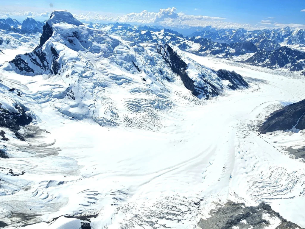 Unforgettable Alaska Flightseeing: A Journey Over Denali National Park 7 Cruising with Danny and Peter, Holland America Line, Westerdam, Anchorage, Alaska, United States | Aerial view of Denali, North America's tallest peak, and the majestic Alaska Range, captured during a Denali National Park flightseeing tour from Anchorage. The image also shows the stunning Ruth Glacier, a specialized plane with skis landing on Denali's snowy terrain, and wildlife such as moose grazing and beluga whales swimming in Cook Inlet.