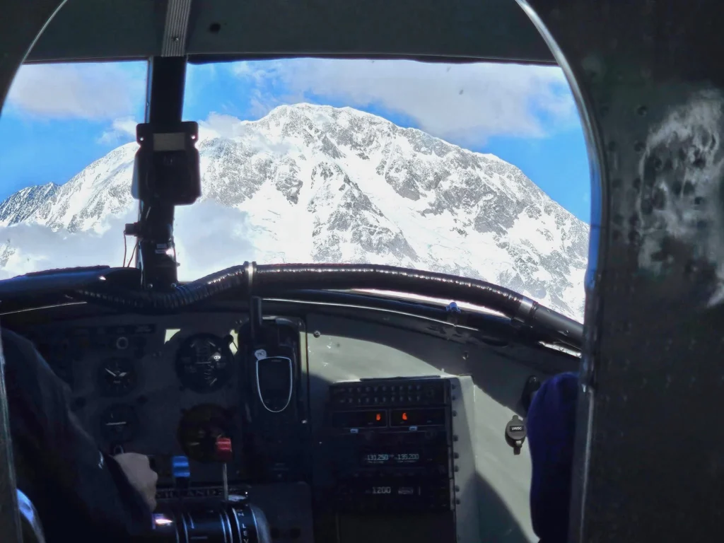 Unforgettable Alaska Flightseeing: A Journey Over Denali National Park 40 Cruising with Danny and Peter, Holland America Line, Westerdam, Anchorage, Alaska, United States | Aerial view of Denali, North America's tallest peak, and the majestic Alaska Range, captured during a Denali National Park flightseeing tour from Anchorage. The image also shows the stunning Ruth Glacier, a specialized plane with skis landing on Denali's snowy terrain, and wildlife such as moose grazing and beluga whales swimming in Cook Inlet.