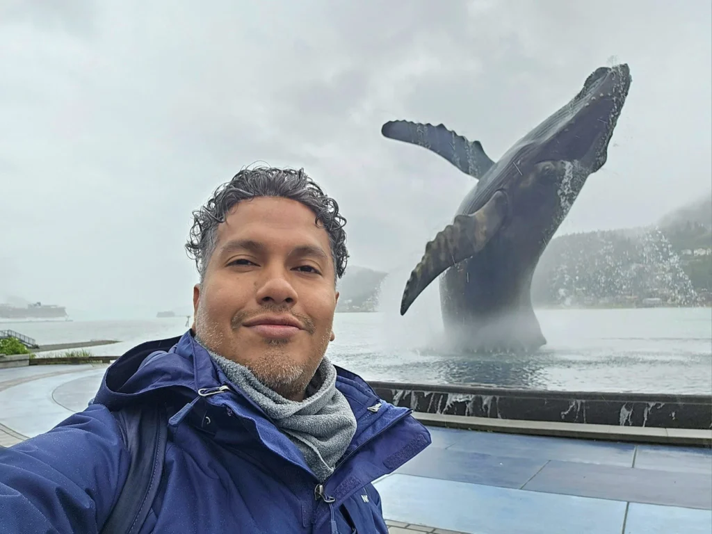 Cruising with Danny and Peter, Holland America Line, Westerdam, Juneau, Alaska, United States | Boat approaching Sentinel Island Lighthouse during Alaska whale watching tour, with humpback whale and stunning coastal scenery in the background.