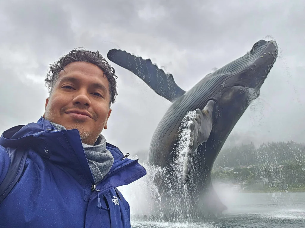 Cruising with Danny and Peter, Holland America Line, Westerdam, Juneau, Alaska, United States | Boat approaching Sentinel Island Lighthouse during Alaska whale watching tour, with humpback whale and stunning coastal scenery in the background.