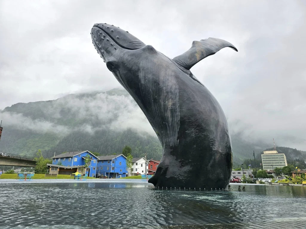 Cruising with Danny and Peter, Holland America Line, Westerdam, Juneau, Alaska, United States | Boat approaching Sentinel Island Lighthouse during Alaska whale watching tour, with humpback whale and stunning coastal scenery in the background.