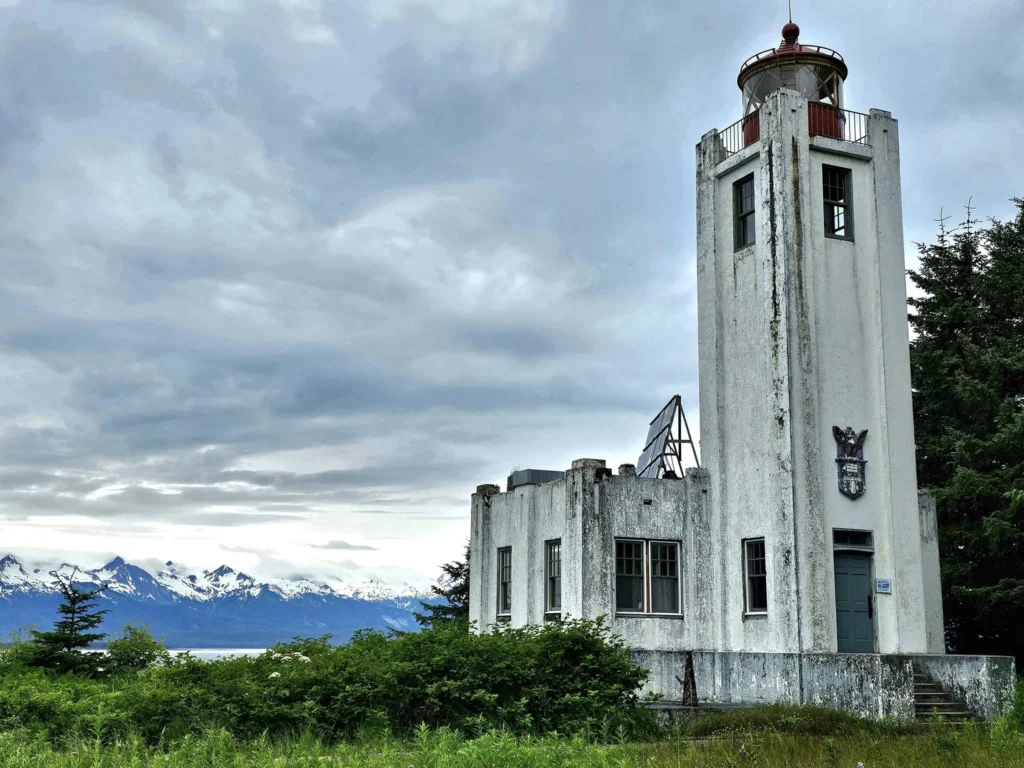 Cruising with Danny and Peter, Holland America Line, Westerdam, Juneau, Alaska, United States | Boat approaching Sentinel Island Lighthouse during Alaska whale watching tour, with humpback whale and stunning coastal scenery in the background.
