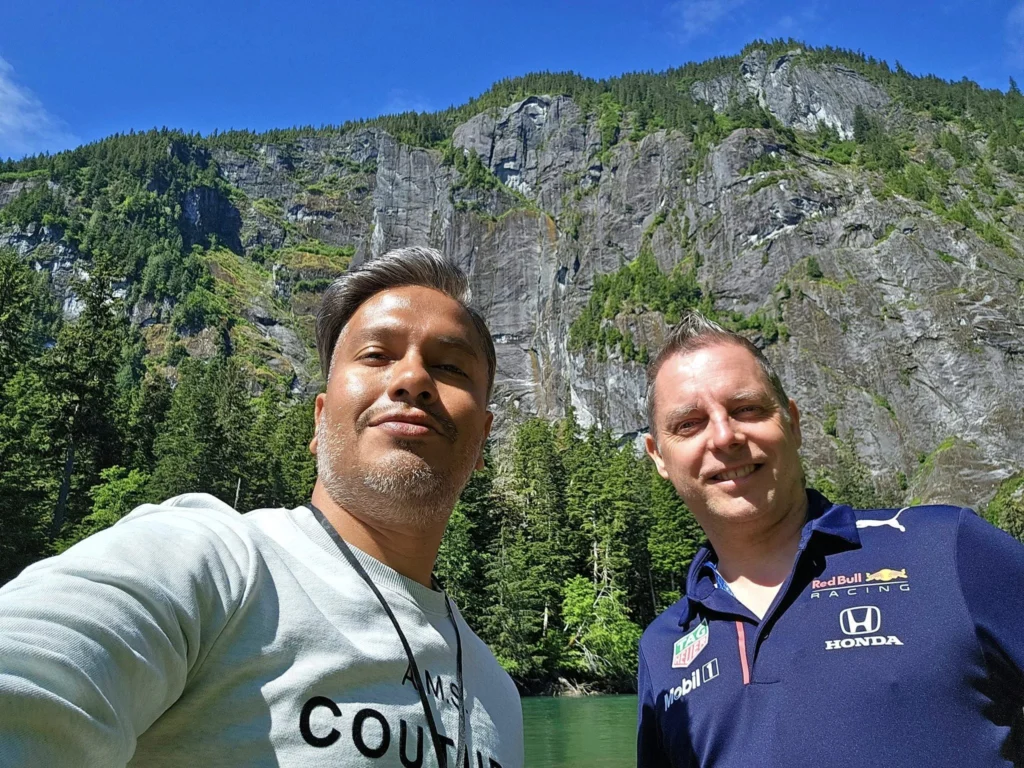 Cruising with Danny and Peter, Holland America Line, Westerdam, Prince Rupert, British Columbia, Canada | In the heart of British Columbia’s wild embrace, Where the Great Bear Rainforest weaves its mystic lace, A journey unfolds, both rail and road in stride, Through nature’s grandeur, where dreams and landscapes collide. From Prince Rupert’s charm, the train departs with grace, A serpentine path through forests’ ancient face, Panoramic windows frame a living, verdant dream, As the Skeena River’s flow whispers its serene theme. Mountains rise like giants, draped in emerald hues, While bald eagles soar, their shadows fleeting views, Black bears wander softly through the forest deep, And mountain goats on rugged cliffs silently leap. Kleanza Creek’s waterfalls cascade with a roar, Nature’s symphony on the rainforest’s floor, And Exchamsiks Park, a jewel of glacial light, Where shimmering pools reflect the day’s pure delight. From rail to road, the scenic drive unveils, A tapestry of mountains and verdant trails, Each turn a canvas painted with the wild’s own hand, A journey through a wonderland, vast and grand. Back in Prince Rupert, where history finds its place, The Museum’s treasures weave a cultural grace, Totem poles and masks tell tales of ancient lore, In this land where the past and present gently soar. Through the Great Bear Rainforest, we wandered wide, In rail and road’s embrace, where nature and culture collide, A journey of wonder, where memories are spun, In the heart of British Columbia, under the sun.