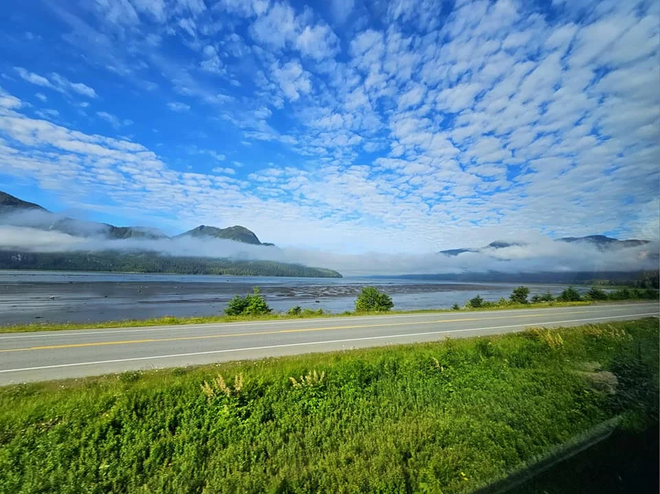 Cruising with Danny and Peter, Holland America Line, Westerdam, Prince Rupert, British Columbia, Canada | In the heart of British Columbia’s wild embrace, Where the Great Bear Rainforest weaves its mystic lace, A journey unfolds, both rail and road in stride, Through nature’s grandeur, where dreams and landscapes collide. From Prince Rupert’s charm, the train departs with grace, A serpentine path through forests’ ancient face, Panoramic windows frame a living, verdant dream, As the Skeena River’s flow whispers its serene theme. Mountains rise like giants, draped in emerald hues, While bald eagles soar, their shadows fleeting views, Black bears wander softly through the forest deep, And mountain goats on rugged cliffs silently leap. Kleanza Creek’s waterfalls cascade with a roar, Nature’s symphony on the rainforest’s floor, And Exchamsiks Park, a jewel of glacial light, Where shimmering pools reflect the day’s pure delight. From rail to road, the scenic drive unveils, A tapestry of mountains and verdant trails, Each turn a canvas painted with the wild’s own hand, A journey through a wonderland, vast and grand. Back in Prince Rupert, where history finds its place, The Museum’s treasures weave a cultural grace, Totem poles and masks tell tales of ancient lore, In this land where the past and present gently soar. Through the Great Bear Rainforest, we wandered wide, In rail and road’s embrace, where nature and culture collide, A journey of wonder, where memories are spun, In the heart of British Columbia, under the sun.