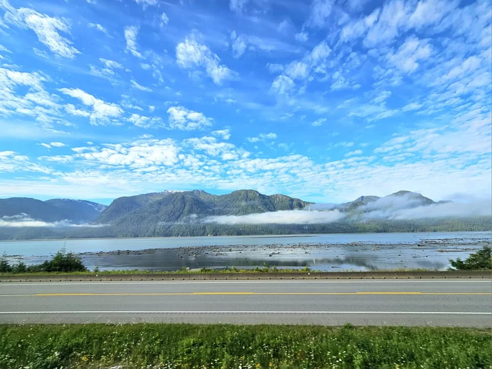 Cruising with Danny and Peter, Holland America Line, Westerdam, Prince Rupert, British Columbia, Canada | In the heart of British Columbia’s wild embrace, Where the Great Bear Rainforest weaves its mystic lace, A journey unfolds, both rail and road in stride, Through nature’s grandeur, where dreams and landscapes collide. From Prince Rupert’s charm, the train departs with grace, A serpentine path through forests’ ancient face, Panoramic windows frame a living, verdant dream, As the Skeena River’s flow whispers its serene theme. Mountains rise like giants, draped in emerald hues, While bald eagles soar, their shadows fleeting views, Black bears wander softly through the forest deep, And mountain goats on rugged cliffs silently leap. Kleanza Creek’s waterfalls cascade with a roar, Nature’s symphony on the rainforest’s floor, And Exchamsiks Park, a jewel of glacial light, Where shimmering pools reflect the day’s pure delight. From rail to road, the scenic drive unveils, A tapestry of mountains and verdant trails, Each turn a canvas painted with the wild’s own hand, A journey through a wonderland, vast and grand. Back in Prince Rupert, where history finds its place, The Museum’s treasures weave a cultural grace, Totem poles and masks tell tales of ancient lore, In this land where the past and present gently soar. Through the Great Bear Rainforest, we wandered wide, In rail and road’s embrace, where nature and culture collide, A journey of wonder, where memories are spun, In the heart of British Columbia, under the sun.