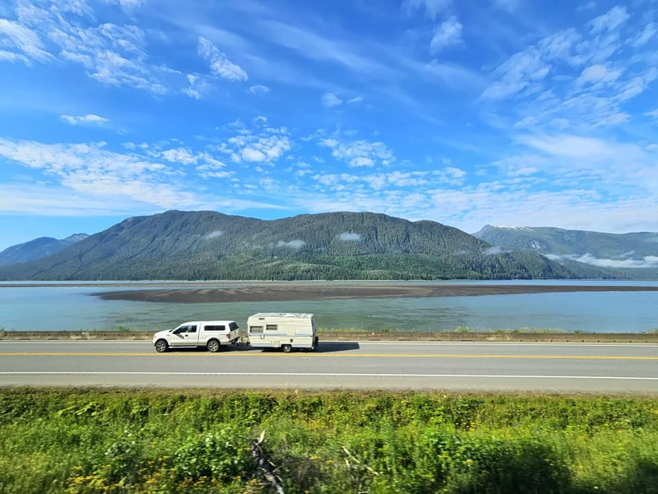 Cruising with Danny and Peter, Holland America Line, Westerdam, Prince Rupert, British Columbia, Canada | In the heart of British Columbia’s wild embrace, Where the Great Bear Rainforest weaves its mystic lace, A journey unfolds, both rail and road in stride, Through nature’s grandeur, where dreams and landscapes collide. From Prince Rupert’s charm, the train departs with grace, A serpentine path through forests’ ancient face, Panoramic windows frame a living, verdant dream, As the Skeena River’s flow whispers its serene theme. Mountains rise like giants, draped in emerald hues, While bald eagles soar, their shadows fleeting views, Black bears wander softly through the forest deep, And mountain goats on rugged cliffs silently leap. Kleanza Creek’s waterfalls cascade with a roar, Nature’s symphony on the rainforest’s floor, And Exchamsiks Park, a jewel of glacial light, Where shimmering pools reflect the day’s pure delight. From rail to road, the scenic drive unveils, A tapestry of mountains and verdant trails, Each turn a canvas painted with the wild’s own hand, A journey through a wonderland, vast and grand. Back in Prince Rupert, where history finds its place, The Museum’s treasures weave a cultural grace, Totem poles and masks tell tales of ancient lore, In this land where the past and present gently soar. Through the Great Bear Rainforest, we wandered wide, In rail and road’s embrace, where nature and culture collide, A journey of wonder, where memories are spun, In the heart of British Columbia, under the sun.