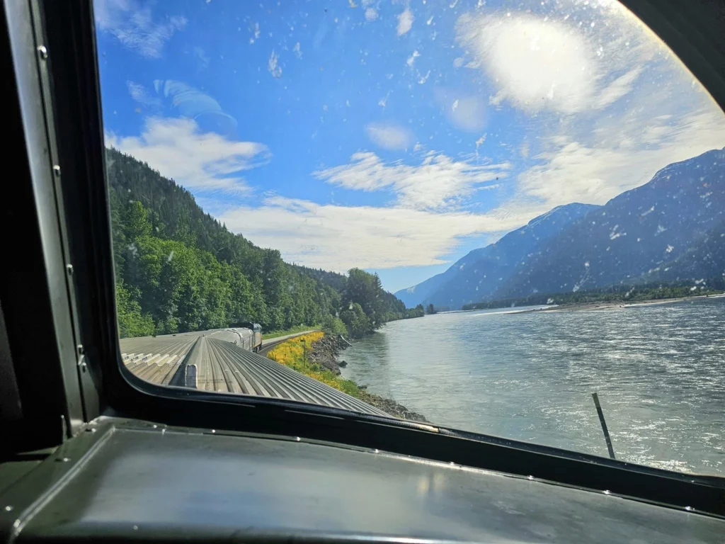 Cruising with Danny and Peter, Holland America Line, Westerdam, Prince Rupert, British Columbia, Canada | In the heart of British Columbia’s wild embrace, Where the Great Bear Rainforest weaves its mystic lace, A journey unfolds, both rail and road in stride, Through nature’s grandeur, where dreams and landscapes collide. From Prince Rupert’s charm, the train departs with grace, A serpentine path through forests’ ancient face, Panoramic windows frame a living, verdant dream, As the Skeena River’s flow whispers its serene theme. Mountains rise like giants, draped in emerald hues, While bald eagles soar, their shadows fleeting views, Black bears wander softly through the forest deep, And mountain goats on rugged cliffs silently leap. Kleanza Creek’s waterfalls cascade with a roar, Nature’s symphony on the rainforest’s floor, And Exchamsiks Park, a jewel of glacial light, Where shimmering pools reflect the day’s pure delight. From rail to road, the scenic drive unveils, A tapestry of mountains and verdant trails, Each turn a canvas painted with the wild’s own hand, A journey through a wonderland, vast and grand. Back in Prince Rupert, where history finds its place, The Museum’s treasures weave a cultural grace, Totem poles and masks tell tales of ancient lore, In this land where the past and present gently soar. Through the Great Bear Rainforest, we wandered wide, In rail and road’s embrace, where nature and culture collide, A journey of wonder, where memories are spun, In the heart of British Columbia, under the sun.