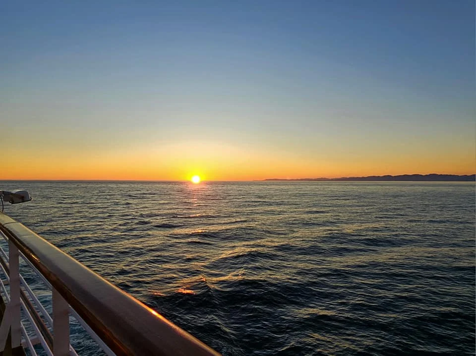 Cruising with Danny and Peter, Holland America Line, Westerdam, Seattle, Washington, United States | Stunning sunset over the ocean during a magical evening cruise from Prince Rupert on the Westerdam, with vibrant orange and pink skies reflecting on calm waters.