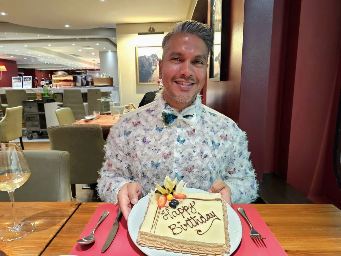 Cruising with Danny and Peter, MSC Cruises, MSC Preziosa, Rotterdam, The Netherlands, Birthday Cruise | The majestic MSC Preziosa cruise ship docked at Rotterdam’s Cruise Terminal on Wilhelminakade, its sleek white exterior gleaming against the modern city skyline with the iconic Erasmus Bridge in the background. Passengers board for a Northern Europe mini-cruise, celebrating a birthday with luxurious touches like a chilled bottle of Spumante and macarons in a stylish cabin. The vibrant onboard atmosphere features a gourmet dining experience at Butcher’s Cut Chef’s Table with a surprise birthday cake, thrilling entertainment at the Platinum Theater’s Rock Nation show with singers and dancers, and a lively Silent Disco in the Safari Lounge. The scene captures the excitement of embarkation day, with scenic views of Rotterdam’s waterfront, onboard shopping for MSC souvenirs, and the promise of an unforgettable luxury cruise vacation.