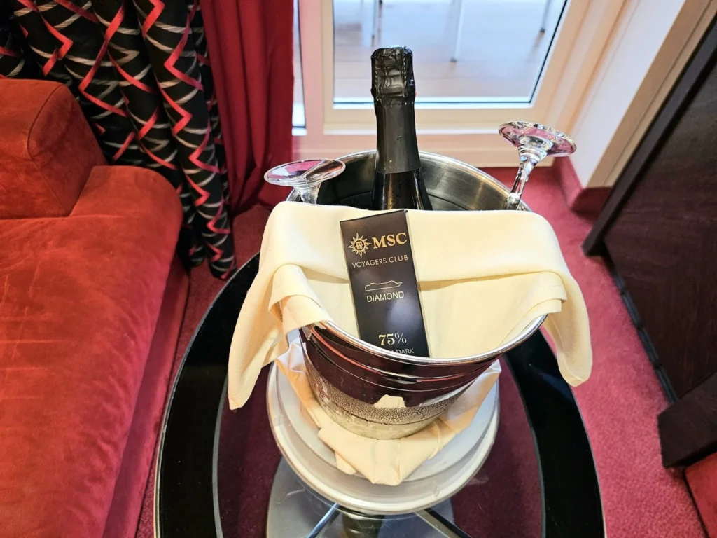 Cruising with Danny and Peter, MSC Cruises, MSC Preziosa, Rotterdam, The Netherlands, Birthday Cruise | The majestic MSC Preziosa cruise ship docked at Rotterdam’s Cruise Terminal on Wilhelminakade, its sleek white exterior gleaming against the modern city skyline with the iconic Erasmus Bridge in the background. Passengers board for a Northern Europe mini-cruise, celebrating a birthday with luxurious touches like a chilled bottle of Spumante and macarons in a stylish cabin. The vibrant onboard atmosphere features a gourmet dining experience at Butcher’s Cut Chef’s Table with a surprise birthday cake, thrilling entertainment at the Platinum Theater’s Rock Nation show with singers and dancers, and a lively Silent Disco in the Safari Lounge. The scene captures the excitement of embarkation day, with scenic views of Rotterdam’s waterfront, onboard shopping for MSC souvenirs, and the promise of an unforgettable luxury cruise vacation.