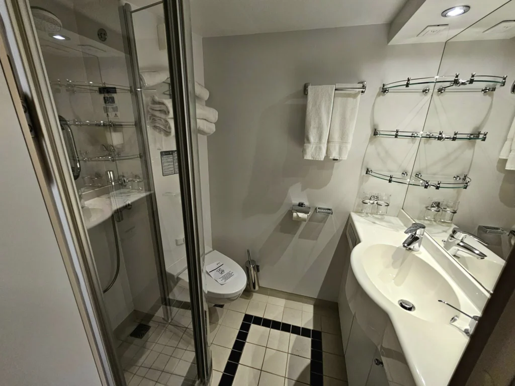 Cruising with Danny and Peter, MSC Cruises, MSC Preziosa, Rotterdam, The Netherlands, Birthday Cruise | The majestic MSC Preziosa cruise ship docked at Rotterdam’s Cruise Terminal on Wilhelminakade, its sleek white exterior gleaming against the modern city skyline with the iconic Erasmus Bridge in the background. Passengers board for a Northern Europe mini-cruise, celebrating a birthday with luxurious touches like a chilled bottle of Spumante and macarons in a stylish cabin. The vibrant onboard atmosphere features a gourmet dining experience at Butcher’s Cut Chef’s Table with a surprise birthday cake, thrilling entertainment at the Platinum Theater’s Rock Nation show with singers and dancers, and a lively Silent Disco in the Safari Lounge. The scene captures the excitement of embarkation day, with scenic views of Rotterdam’s waterfront, onboard shopping for MSC souvenirs, and the promise of an unforgettable luxury cruise vacation.