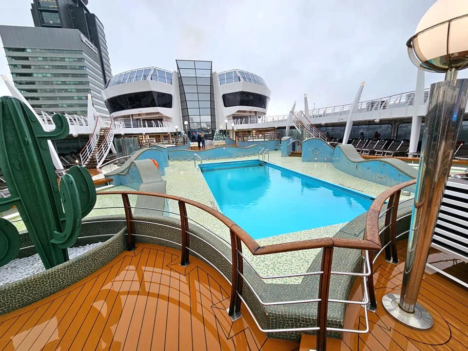 Cruising with Danny and Peter, MSC Cruises, MSC Preziosa, Rotterdam, The Netherlands, Birthday Cruise | The majestic MSC Preziosa cruise ship docked at Rotterdam’s Cruise Terminal on Wilhelminakade, its sleek white exterior gleaming against the modern city skyline with the iconic Erasmus Bridge in the background. Passengers board for a Northern Europe mini-cruise, celebrating a birthday with luxurious touches like a chilled bottle of Spumante and macarons in a stylish cabin. The vibrant onboard atmosphere features a gourmet dining experience at Butcher’s Cut Chef’s Table with a surprise birthday cake, thrilling entertainment at the Platinum Theater’s Rock Nation show with singers and dancers, and a lively Silent Disco in the Safari Lounge. The scene captures the excitement of embarkation day, with scenic views of Rotterdam’s waterfront, onboard shopping for MSC souvenirs, and the promise of an unforgettable luxury cruise vacation.