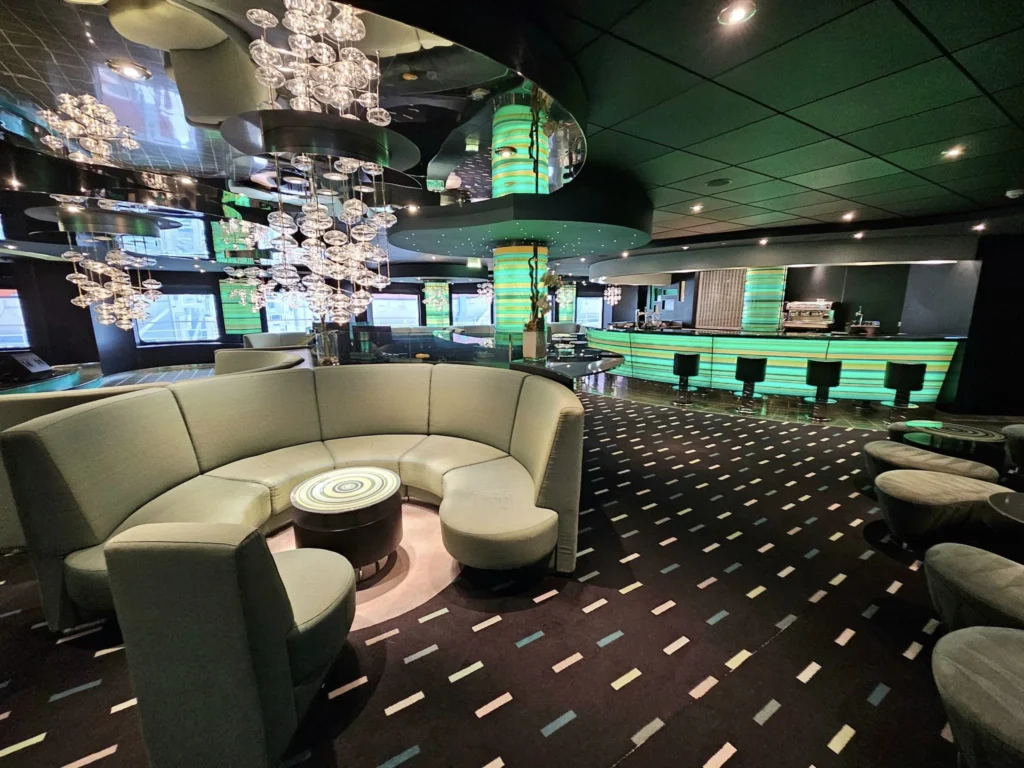 Cruising with Danny and Peter, MSC Cruises, MSC Preziosa, Rotterdam, The Netherlands, Birthday Cruise | The majestic MSC Preziosa cruise ship docked at Rotterdam’s Cruise Terminal on Wilhelminakade, its sleek white exterior gleaming against the modern city skyline with the iconic Erasmus Bridge in the background. Passengers board for a Northern Europe mini-cruise, celebrating a birthday with luxurious touches like a chilled bottle of Spumante and macarons in a stylish cabin. The vibrant onboard atmosphere features a gourmet dining experience at Butcher’s Cut Chef’s Table with a surprise birthday cake, thrilling entertainment at the Platinum Theater’s Rock Nation show with singers and dancers, and a lively Silent Disco in the Safari Lounge. The scene captures the excitement of embarkation day, with scenic views of Rotterdam’s waterfront, onboard shopping for MSC souvenirs, and the promise of an unforgettable luxury cruise vacation.