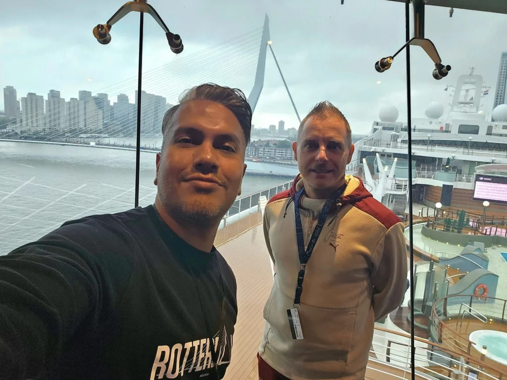 Cruising with Danny and Peter, MSC Cruises, MSC Preziosa, Rotterdam, The Netherlands, Birthday Cruise | The majestic MSC Preziosa cruise ship docked at Rotterdam’s Cruise Terminal on Wilhelminakade, its sleek white exterior gleaming against the modern city skyline with the iconic Erasmus Bridge in the background. Passengers board for a Northern Europe mini-cruise, celebrating a birthday with luxurious touches like a chilled bottle of Spumante and macarons in a stylish cabin. The vibrant onboard atmosphere features a gourmet dining experience at Butcher’s Cut Chef’s Table with a surprise birthday cake, thrilling entertainment at the Platinum Theater’s Rock Nation show with singers and dancers, and a lively Silent Disco in the Safari Lounge. The scene captures the excitement of embarkation day, with scenic views of Rotterdam’s waterfront, onboard shopping for MSC souvenirs, and the promise of an unforgettable luxury cruise vacation.