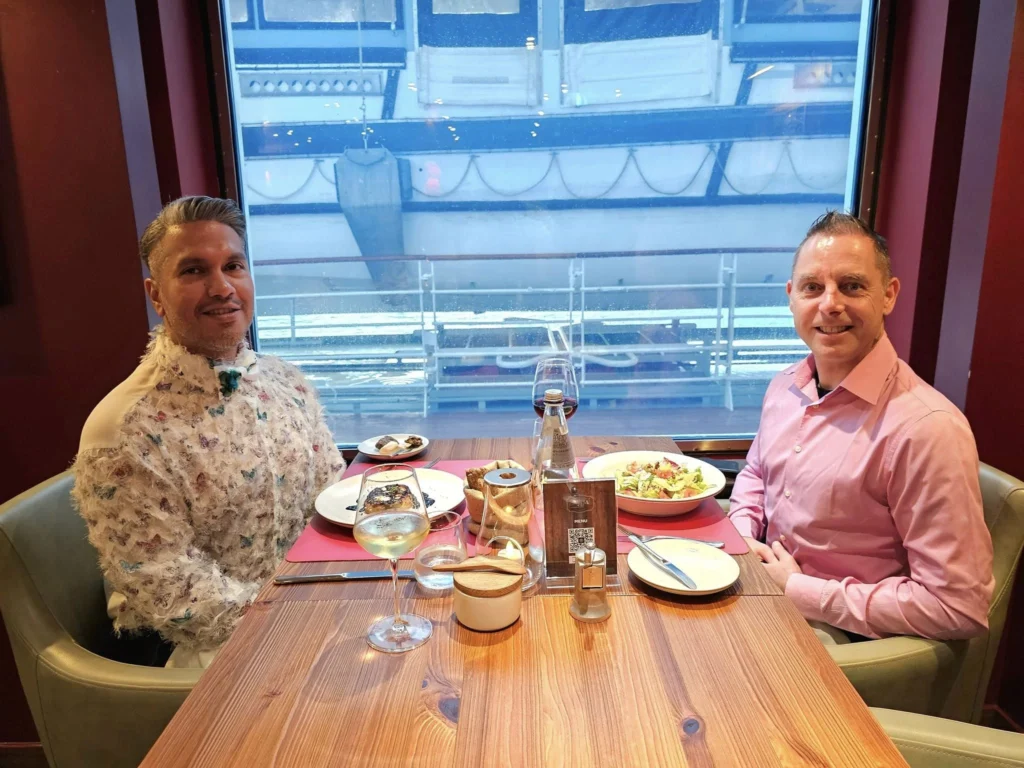 Cruising with Danny and Peter, MSC Cruises, MSC Preziosa, Rotterdam, The Netherlands, Birthday Cruise | The majestic MSC Preziosa cruise ship docked at Rotterdam’s Cruise Terminal on Wilhelminakade, its sleek white exterior gleaming against the modern city skyline with the iconic Erasmus Bridge in the background. Passengers board for a Northern Europe mini-cruise, celebrating a birthday with luxurious touches like a chilled bottle of Spumante and macarons in a stylish cabin. The vibrant onboard atmosphere features a gourmet dining experience at Butcher’s Cut Chef’s Table with a surprise birthday cake, thrilling entertainment at the Platinum Theater’s Rock Nation show with singers and dancers, and a lively Silent Disco in the Safari Lounge. The scene captures the excitement of embarkation day, with scenic views of Rotterdam’s waterfront, onboard shopping for MSC souvenirs, and the promise of an unforgettable luxury cruise vacation.