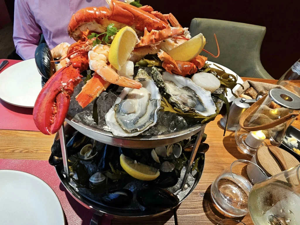 Cruising with Danny and Peter, MSC Cruises, MSC Preziosa, Rotterdam, The Netherlands, Birthday Cruise | The majestic MSC Preziosa cruise ship docked at Rotterdam’s Cruise Terminal on Wilhelminakade, its sleek white exterior gleaming against the modern city skyline with the iconic Erasmus Bridge in the background. Passengers board for a Northern Europe mini-cruise, celebrating a birthday with luxurious touches like a chilled bottle of Spumante and macarons in a stylish cabin. The vibrant onboard atmosphere features a gourmet dining experience at Butcher’s Cut Chef’s Table with a surprise birthday cake, thrilling entertainment at the Platinum Theater’s Rock Nation show with singers and dancers, and a lively Silent Disco in the Safari Lounge. The scene captures the excitement of embarkation day, with scenic views of Rotterdam’s waterfront, onboard shopping for MSC souvenirs, and the promise of an unforgettable luxury cruise vacation.