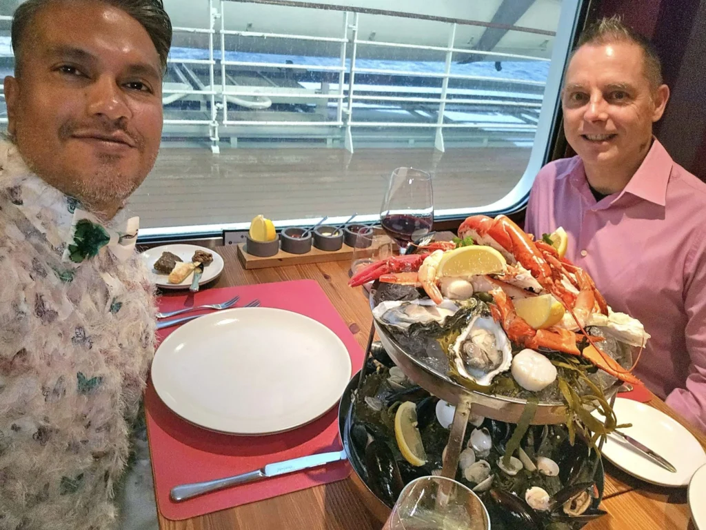 Cruising with Danny and Peter, MSC Cruises, MSC Preziosa, Rotterdam, The Netherlands, Birthday Cruise | The majestic MSC Preziosa cruise ship docked at Rotterdam’s Cruise Terminal on Wilhelminakade, its sleek white exterior gleaming against the modern city skyline with the iconic Erasmus Bridge in the background. Passengers board for a Northern Europe mini-cruise, celebrating a birthday with luxurious touches like a chilled bottle of Spumante and macarons in a stylish cabin. The vibrant onboard atmosphere features a gourmet dining experience at Butcher’s Cut Chef’s Table with a surprise birthday cake, thrilling entertainment at the Platinum Theater’s Rock Nation show with singers and dancers, and a lively Silent Disco in the Safari Lounge. The scene captures the excitement of embarkation day, with scenic views of Rotterdam’s waterfront, onboard shopping for MSC souvenirs, and the promise of an unforgettable luxury cruise vacation.