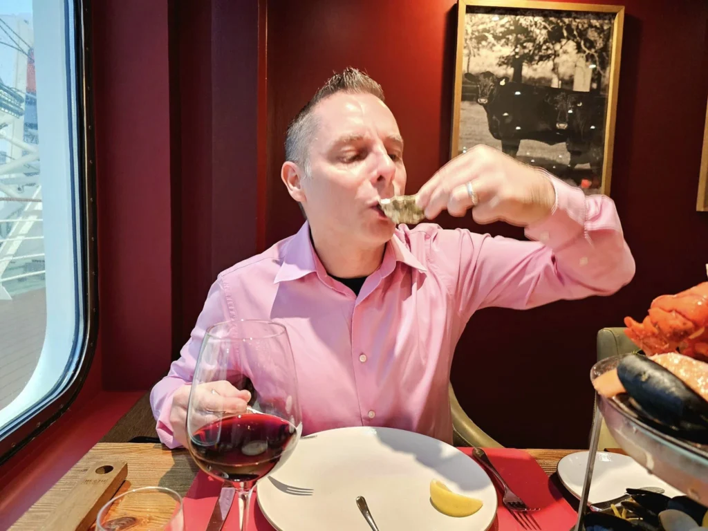 Cruising with Danny and Peter, MSC Cruises, MSC Preziosa, Rotterdam, The Netherlands, Birthday Cruise | The majestic MSC Preziosa cruise ship docked at Rotterdam’s Cruise Terminal on Wilhelminakade, its sleek white exterior gleaming against the modern city skyline with the iconic Erasmus Bridge in the background. Passengers board for a Northern Europe mini-cruise, celebrating a birthday with luxurious touches like a chilled bottle of Spumante and macarons in a stylish cabin. The vibrant onboard atmosphere features a gourmet dining experience at Butcher’s Cut Chef’s Table with a surprise birthday cake, thrilling entertainment at the Platinum Theater’s Rock Nation show with singers and dancers, and a lively Silent Disco in the Safari Lounge. The scene captures the excitement of embarkation day, with scenic views of Rotterdam’s waterfront, onboard shopping for MSC souvenirs, and the promise of an unforgettable luxury cruise vacation.