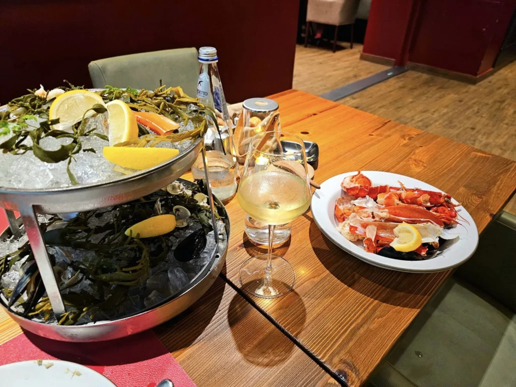 Cruising with Danny and Peter, MSC Cruises, MSC Preziosa, Rotterdam, The Netherlands, Birthday Cruise | The majestic MSC Preziosa cruise ship docked at Rotterdam’s Cruise Terminal on Wilhelminakade, its sleek white exterior gleaming against the modern city skyline with the iconic Erasmus Bridge in the background. Passengers board for a Northern Europe mini-cruise, celebrating a birthday with luxurious touches like a chilled bottle of Spumante and macarons in a stylish cabin. The vibrant onboard atmosphere features a gourmet dining experience at Butcher’s Cut Chef’s Table with a surprise birthday cake, thrilling entertainment at the Platinum Theater’s Rock Nation show with singers and dancers, and a lively Silent Disco in the Safari Lounge. The scene captures the excitement of embarkation day, with scenic views of Rotterdam’s waterfront, onboard shopping for MSC souvenirs, and the promise of an unforgettable luxury cruise vacation.