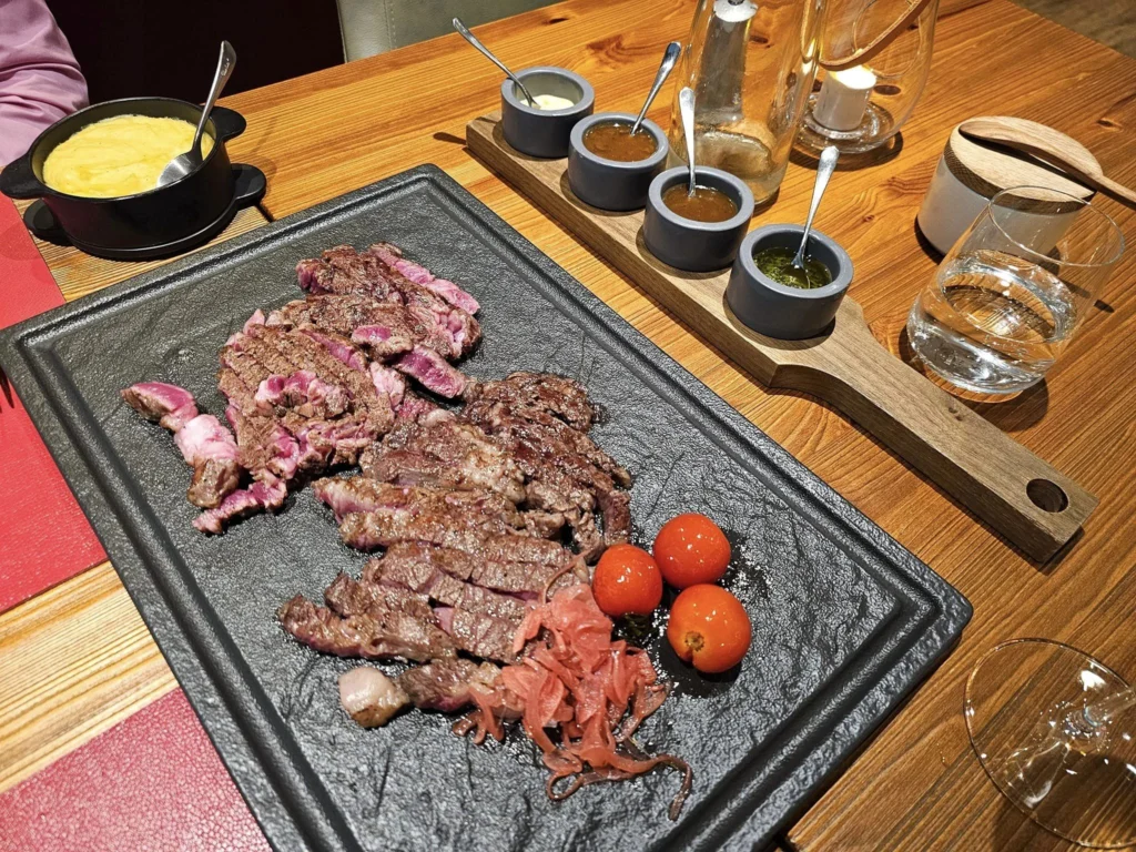 Cruising with Danny and Peter, MSC Cruises, MSC Preziosa, Rotterdam, The Netherlands, Birthday Cruise | The majestic MSC Preziosa cruise ship docked at Rotterdam’s Cruise Terminal on Wilhelminakade, its sleek white exterior gleaming against the modern city skyline with the iconic Erasmus Bridge in the background. Passengers board for a Northern Europe mini-cruise, celebrating a birthday with luxurious touches like a chilled bottle of Spumante and macarons in a stylish cabin. The vibrant onboard atmosphere features a gourmet dining experience at Butcher’s Cut Chef’s Table with a surprise birthday cake, thrilling entertainment at the Platinum Theater’s Rock Nation show with singers and dancers, and a lively Silent Disco in the Safari Lounge. The scene captures the excitement of embarkation day, with scenic views of Rotterdam’s waterfront, onboard shopping for MSC souvenirs, and the promise of an unforgettable luxury cruise vacation.