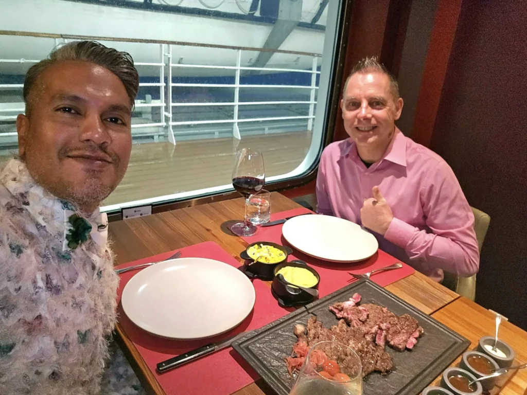 Cruising with Danny and Peter, MSC Cruises, MSC Preziosa, Rotterdam, The Netherlands, Birthday Cruise | The majestic MSC Preziosa cruise ship docked at Rotterdam’s Cruise Terminal on Wilhelminakade, its sleek white exterior gleaming against the modern city skyline with the iconic Erasmus Bridge in the background. Passengers board for a Northern Europe mini-cruise, celebrating a birthday with luxurious touches like a chilled bottle of Spumante and macarons in a stylish cabin. The vibrant onboard atmosphere features a gourmet dining experience at Butcher’s Cut Chef’s Table with a surprise birthday cake, thrilling entertainment at the Platinum Theater’s Rock Nation show with singers and dancers, and a lively Silent Disco in the Safari Lounge. The scene captures the excitement of embarkation day, with scenic views of Rotterdam’s waterfront, onboard shopping for MSC souvenirs, and the promise of an unforgettable luxury cruise vacation.