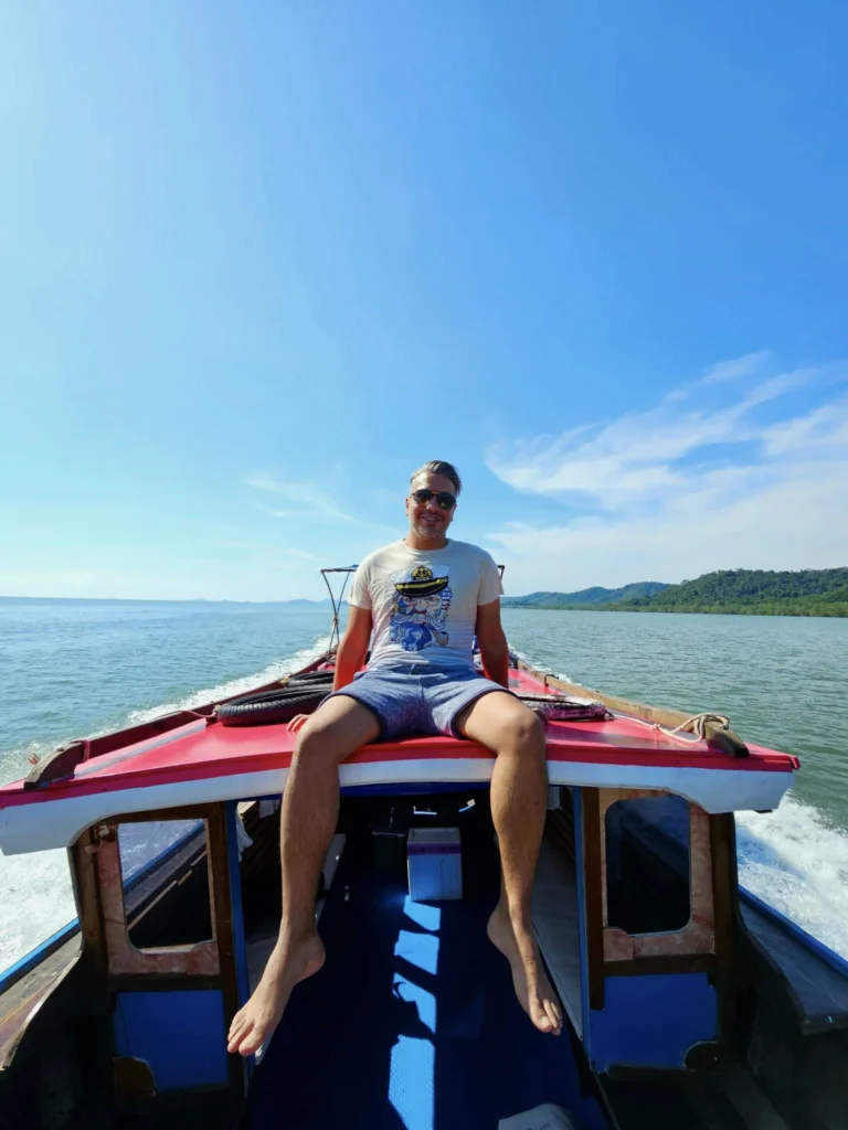 Cruising with Danny and Peter, Holland America Line, Westerdam, Phuket, Thailand | Longtail boat navigating clear waters near James Bond Island, showcasing iconic limestone cliffs. Enjoy dining at a floating restaurant on Phang Nga Bay, kayaking through lush mangroves, and exploring hidden caves with unique rock formations during an unforgettable Phuket island tour.