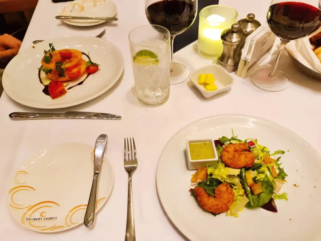 Cruising with Danny and Peter, Holland America Line, Koningsdam, Pacific Ocean, Sea Day | Passengers enjoying a tranquil Holland America sea day aboard a luxury cruise ship, participating in ocean voyage activities such as ukulele lessons, savoring gourmet dining at sea, and relaxing by the pool while overlooking the serene waters. The elegant ship provides panoramic ocean views and a perfect setting for a memorable Holland America Line experience. The day also includes presentations on maritime history, reflecting the ultimate luxury travel experience at sea.