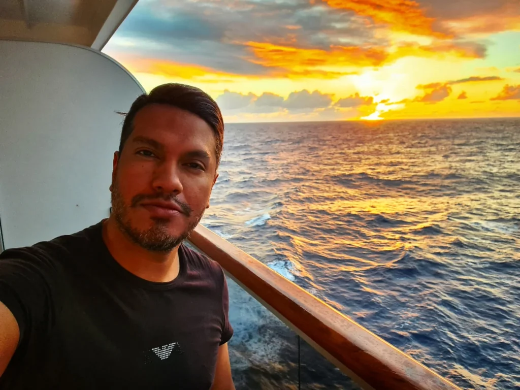 Cruising with Danny and Peter, Holland America Line, Koningsdam, Pacific Ocean, Sea Day | A stunning sunrise over the ocean during a Hawaiian cruise, showcasing the vibrant colors of the sky, a luxury cruise ship on calm waters, guests enjoying marine biology lectures, participating in ukulele lessons, and savoring delicious culinary experiences, embodying relaxation and adventure at sea in the beautiful Hawaiian Islands.