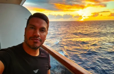 Cruising with Danny and Peter, Holland America Line, Koningsdam, Pacific Ocean, Sea Day | A stunning sunrise over the ocean during a Hawaiian cruise, showcasing the vibrant colors of the sky, a luxury cruise ship on calm waters, guests enjoying marine biology lectures, participating in ukulele lessons, and savoring delicious culinary experiences, embodying relaxation and adventure at sea in the beautiful Hawaiian Islands.