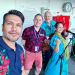 Cruising with Danny and Peter, Holland America Line, Koningsdam, Pacific Ocean, Sea Day | Group of travelers enjoying ukulele lessons on the deck of a cruise ship during an ocean voyage. Vibrant sunset over the sea, showcasing the essence of Hawaiian culture. Participants performing in a live music at sea event, celebrating their ukulele performances together, surrounded by the beauty of the ocean and the warmth of camaraderie.