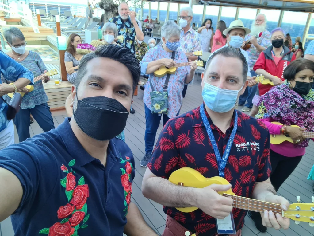 Cruising with Danny and Peter, Holland America Line, Koningsdam, Pacific Ocean, Sea Day | Group of travelers enjoying ukulele lessons on the deck of a cruise ship during an ocean voyage. Vibrant sunset over the sea, showcasing the essence of Hawaiian culture. Participants performing in a live music at sea event, celebrating their ukulele performances together, surrounded by the beauty of the ocean and the warmth of camaraderie.