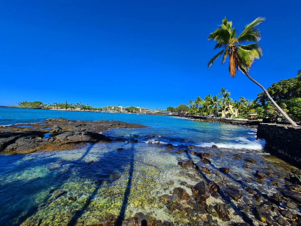 Cruising with Danny and Peter, Holland America Line, Koningsdam, Kona, Hawaii, United-States | A vibrant scene showcasing the beauty of Kona Hawaii, featuring secluded beaches with soft sand and crystal-clear waters, colorful storefronts along the bustling streets, and breathtaking scenic views of the Kona coast during sunset. The image captures the essence of Exploring Kona's Island Charm, highlighting local culture with hula dancers and delicious Hawaiian cuisine served at a beachfront restaurant.