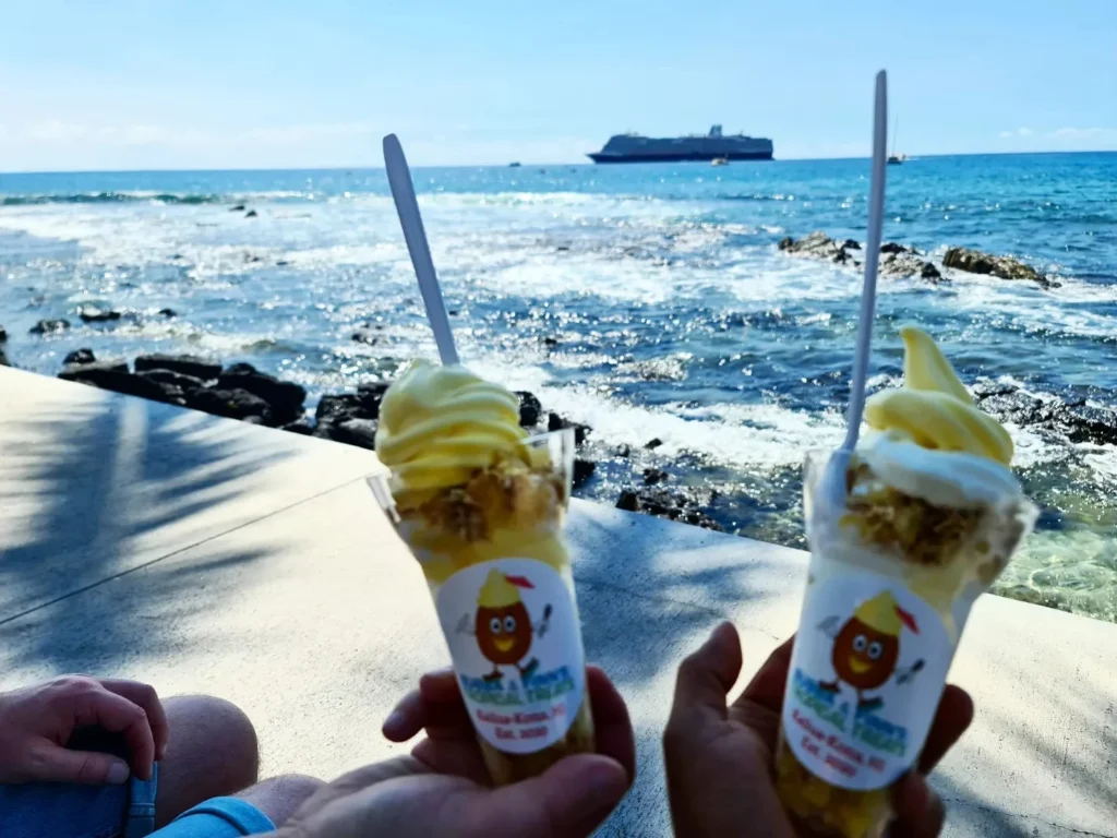 Cruising with Danny and Peter, Holland America Line, Koningsdam, Kona, Hawaii, United-States | A vibrant scene showcasing the beauty of Kona Hawaii, featuring secluded beaches with soft sand and crystal-clear waters, colorful storefronts along the bustling streets, and breathtaking scenic views of the Kona coast during sunset. The image captures the essence of Exploring Kona's Island Charm, highlighting local culture with hula dancers and delicious Hawaiian cuisine served at a beachfront restaurant.