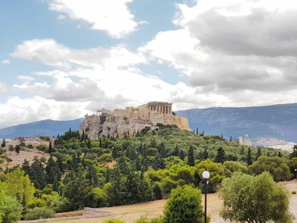 Cruising with Danny and Peter, Holland America Line, Koningsdam, Piraeus, Athens, Greece | A vibrant street art mural in Athens, showcasing the city's artistic spirit, with the Acropolis in the background; a local café offering panoramic views, perfect for an Athens Instagram Tour; hidden gems of Athens, including narrow alleys and quaint courtyards filled with history and charm.