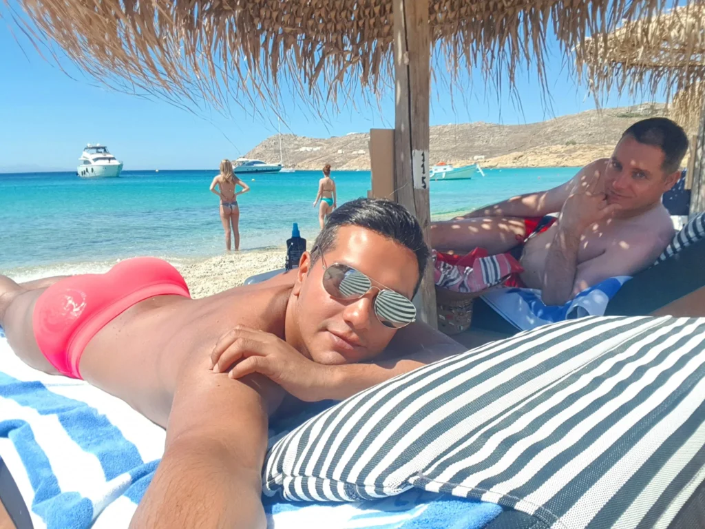 Cruising with Danny and Peter, Holland America Line, Koningsdam, Mykonos, Greece | Scenic view of Elia Beach in Mykonos, showcasing crystal-clear waters, soft sands, and the stunning Aegean Sea backdrop, with travelers enjoying their Mykonos Greece travel experience, exploring the serene beach and vibrant Mykonos Town attractions.