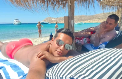 Cruising with Danny and Peter, Holland America Line, Koningsdam, Mykonos, Greece | Scenic view of Elia Beach in Mykonos, showcasing crystal-clear waters, soft sands, and the stunning Aegean Sea backdrop, with travelers enjoying their Mykonos Greece travel experience, exploring the serene beach and vibrant Mykonos Town attractions.