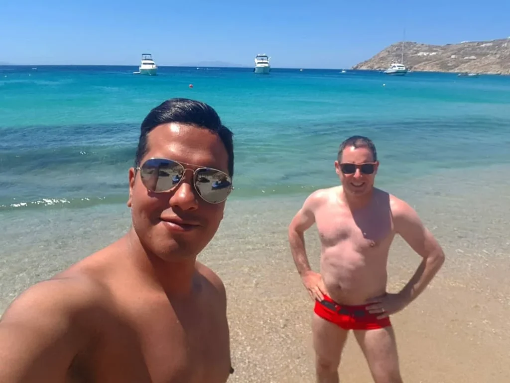 Cruising with Danny and Peter, Holland America Line, Koningsdam, Mykonos, Greece | Scenic view of Elia Beach in Mykonos, showcasing crystal-clear waters, soft sands, and the stunning Aegean Sea backdrop, with travelers enjoying their Mykonos Greece travel experience, exploring the serene beach and vibrant Mykonos Town attractions.