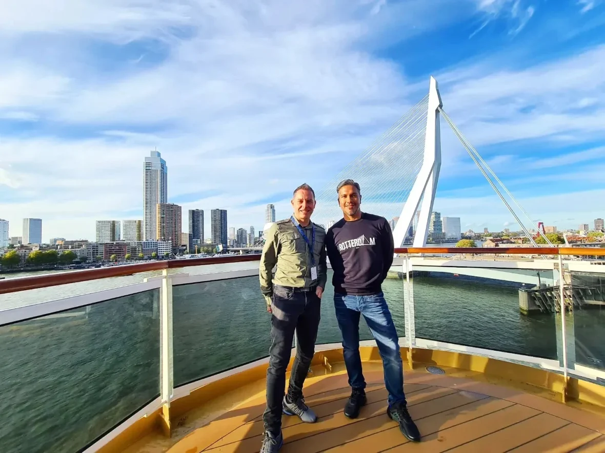 Cruising with Danny and Peter, Holland America Line, Rotterdam, Rotterdam, The Netherlands | A stunning view of the M.S. Rotterdam as it sails away from Rotterdam, celebrating Holland America 150th Anniversary with historic ships in the background. The sunset casts a golden glow on the luxury ocean liner, capturing the excitement of our transatlantic voyage from Rotterdam to New York. A special anniversary menu and Holland America memorabilia highlight this remarkable journey.