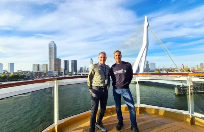 Cruising with Danny and Peter, Holland America Line, Rotterdam, Rotterdam, The Netherlands | A stunning view of the M.S. Rotterdam as it sails away from Rotterdam, celebrating Holland America 150th Anniversary with historic ships in the background. The sunset casts a golden glow on the luxury ocean liner, capturing the excitement of our transatlantic voyage from Rotterdam to New York. A special anniversary menu and Holland America memorabilia highlight this remarkable journey.