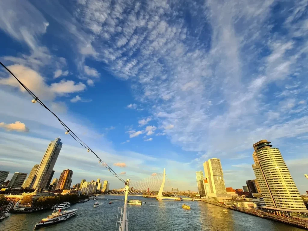 Cruising with Danny and Peter, Holland America Line, Rotterdam, Rotterdam, The Netherlands | A stunning view of the M.S. Rotterdam as it sails away from Rotterdam, celebrating Holland America 150th Anniversary with historic ships in the background. The sunset casts a golden glow on the luxury ocean liner, capturing the excitement of our transatlantic voyage from Rotterdam to New York. A special anniversary menu and Holland America memorabilia highlight this remarkable journey.