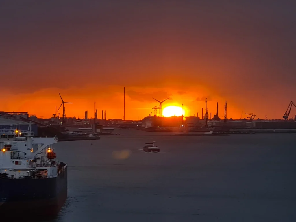 Cruising with Danny and Peter, Holland America Line, Rotterdam, Rotterdam, The Netherlands | A stunning view of the M.S. Rotterdam as it sails away from Rotterdam, celebrating Holland America 150th Anniversary with historic ships in the background. The sunset casts a golden glow on the luxury ocean liner, capturing the excitement of our transatlantic voyage from Rotterdam to New York. A special anniversary menu and Holland America memorabilia highlight this remarkable journey.