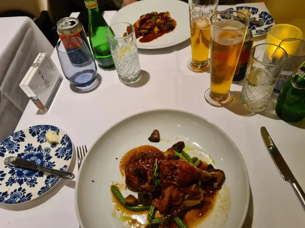 Cruising with Danny and Peter, Holland America Line, Rotterdam, Rotterdam, The Netherlands | A stunning view of the M.S. Rotterdam as it sails away from Rotterdam, celebrating Holland America 150th Anniversary with historic ships in the background. The sunset casts a golden glow on the luxury ocean liner, capturing the excitement of our transatlantic voyage from Rotterdam to New York. A special anniversary menu and Holland America memorabilia highlight this remarkable journey.