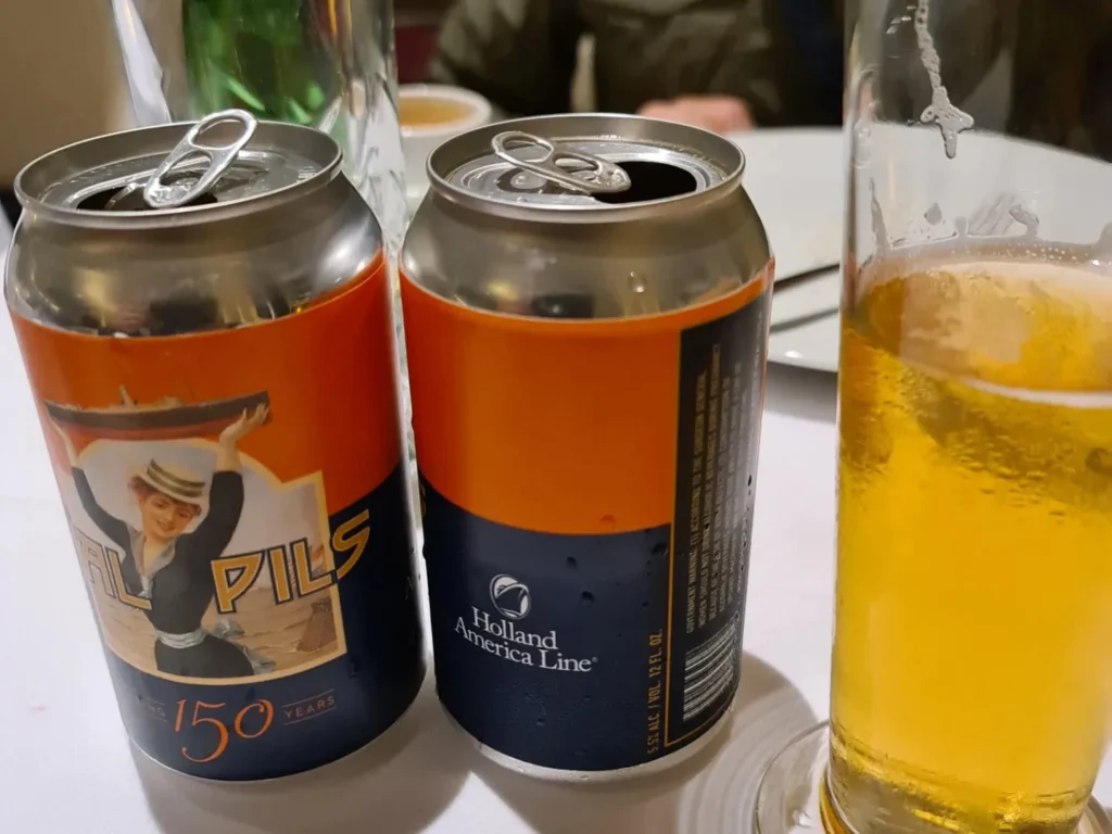 Cruising with Danny and Peter, Holland America Line, Rotterdam, Rotterdam, The Netherlands | A stunning view of the M.S. Rotterdam as it sails away from Rotterdam, celebrating Holland America 150th Anniversary with historic ships in the background. The sunset casts a golden glow on the luxury ocean liner, capturing the excitement of our transatlantic voyage from Rotterdam to New York. A special anniversary menu and Holland America memorabilia highlight this remarkable journey.