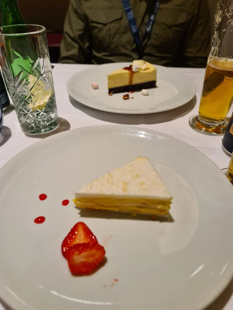 Cruising with Danny and Peter, Holland America Line, Rotterdam, Rotterdam, The Netherlands | A stunning view of the M.S. Rotterdam as it sails away from Rotterdam, celebrating Holland America 150th Anniversary with historic ships in the background. The sunset casts a golden glow on the luxury ocean liner, capturing the excitement of our transatlantic voyage from Rotterdam to New York. A special anniversary menu and Holland America memorabilia highlight this remarkable journey.