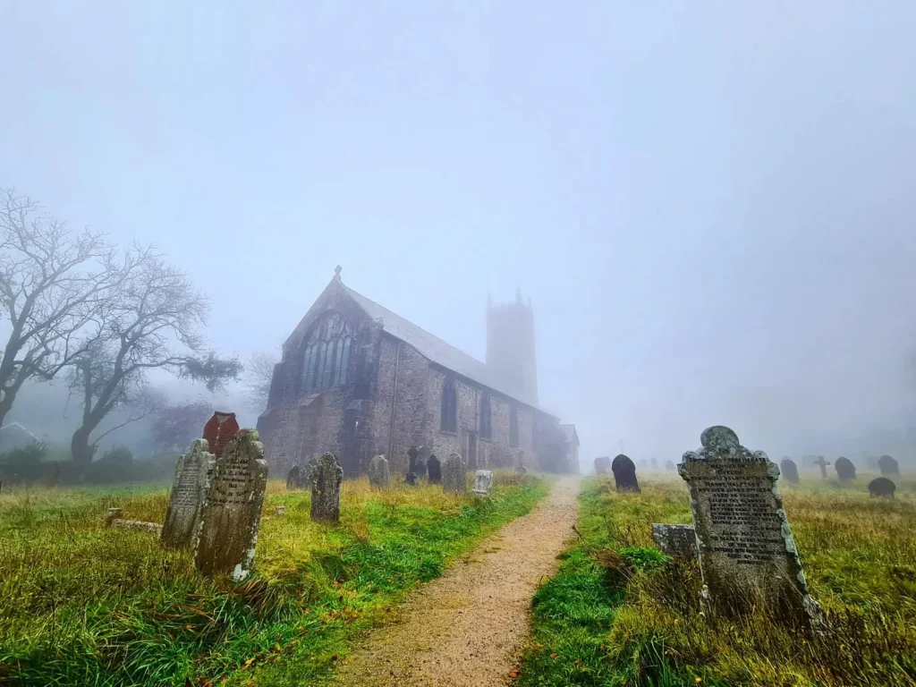 Cruising with Danny and Peter, Holland America Line, Rotterdam, Plymouth, England, Great Britain, United Kingdom | A foggy day in Plymouth Dartmoor showcases an eerie scene of historic churches and spooky graveyards, highlighting the enchanting beauty of Plymouth UK travel. A winding hiking trail through Dartmoor National Park is visible, surrounded by lush greenery and misty landscapes.