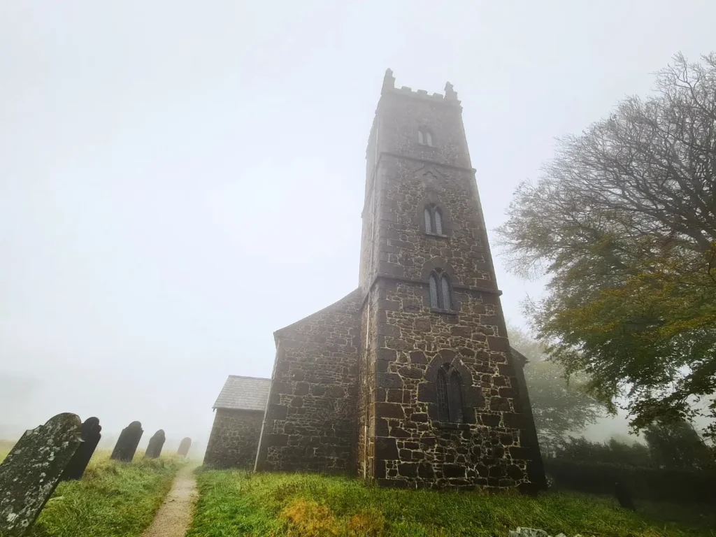 Cruising with Danny and Peter, Holland America Line, Rotterdam, Plymouth, England, Great Britain, United Kingdom | A foggy day in Plymouth Dartmoor showcases an eerie scene of historic churches and spooky graveyards, highlighting the enchanting beauty of Plymouth UK travel. A winding hiking trail through Dartmoor National Park is visible, surrounded by lush greenery and misty landscapes.