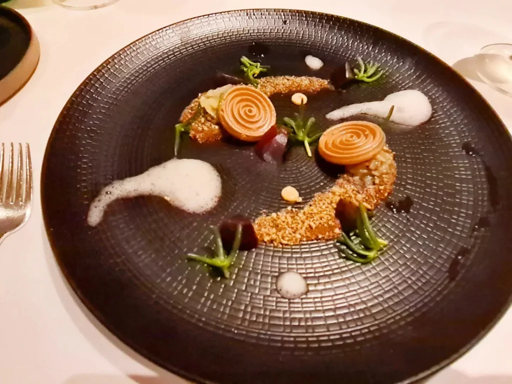 Cruising with Danny and Peter, Holland America Line, Rotterdam, Atlantic Ocean, Sea Day | A beautifully plated dish from the Taste of De Librije dinner aboard the Rotterdam, featuring Jonnie Boer cuisine, including caviar egg, king fish, and oysters, paired with Cloudy Bay Sauvignon Blanc. The elegant dining setup highlights the luxurious atmosphere of Holland America Line's Pinnacle Grill during this exquisite transatlantic cruise dinner.