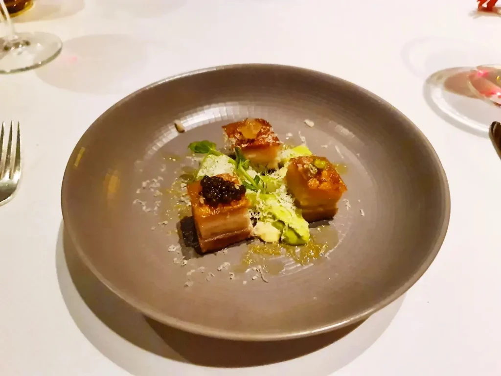 Cruising with Danny and Peter, Holland America Line, Rotterdam, Atlantic Ocean, Sea Day | A beautifully plated dish from the Taste of De Librije dinner aboard the Rotterdam, featuring Jonnie Boer cuisine, including caviar egg, king fish, and oysters, paired with Cloudy Bay Sauvignon Blanc. The elegant dining setup highlights the luxurious atmosphere of Holland America Line's Pinnacle Grill during this exquisite transatlantic cruise dinner.